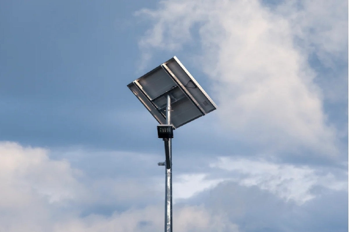 A large panel and a small rectangular light mounted on a pole beneath a cloudy sky.