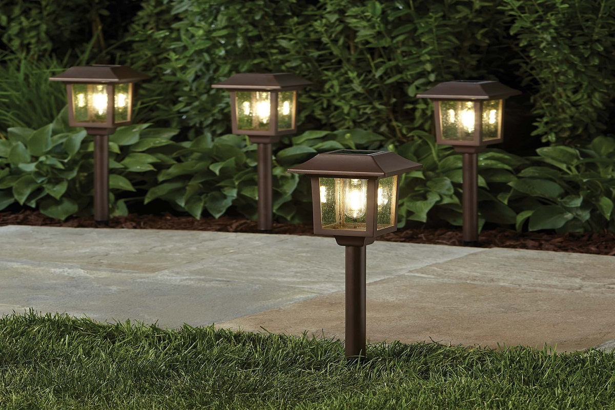 Four glowing lantern-style path lights beside paving, grass and shrubs.